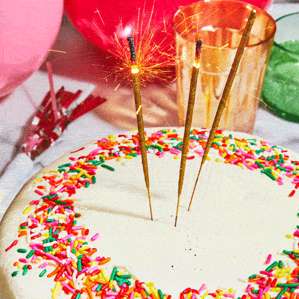Three sparkler candles burning on a Sugaree’s Rainbow Cake with sprinkles