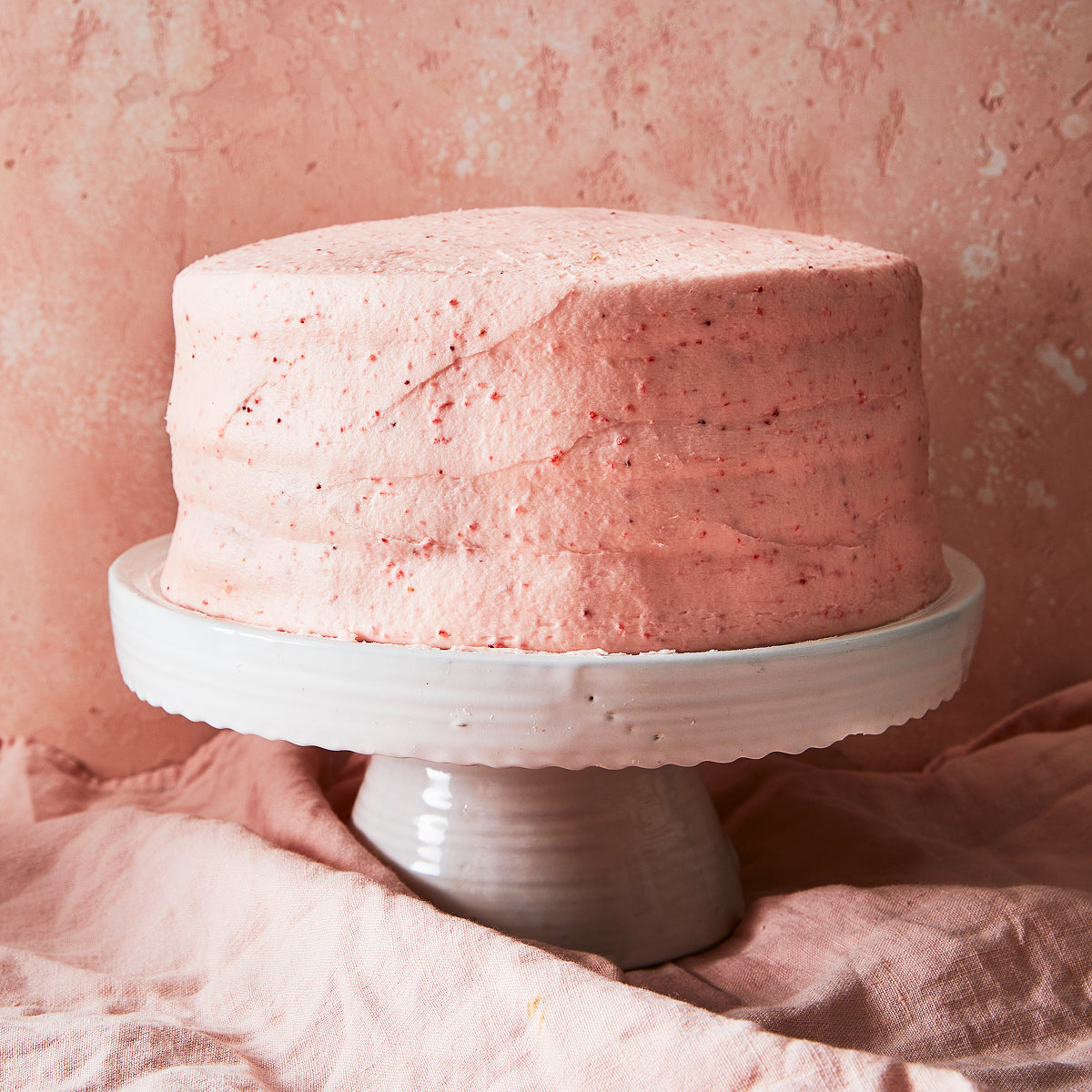 Pink Sugaree’s Strawberry Cake on a white cake stand against a pink textured background