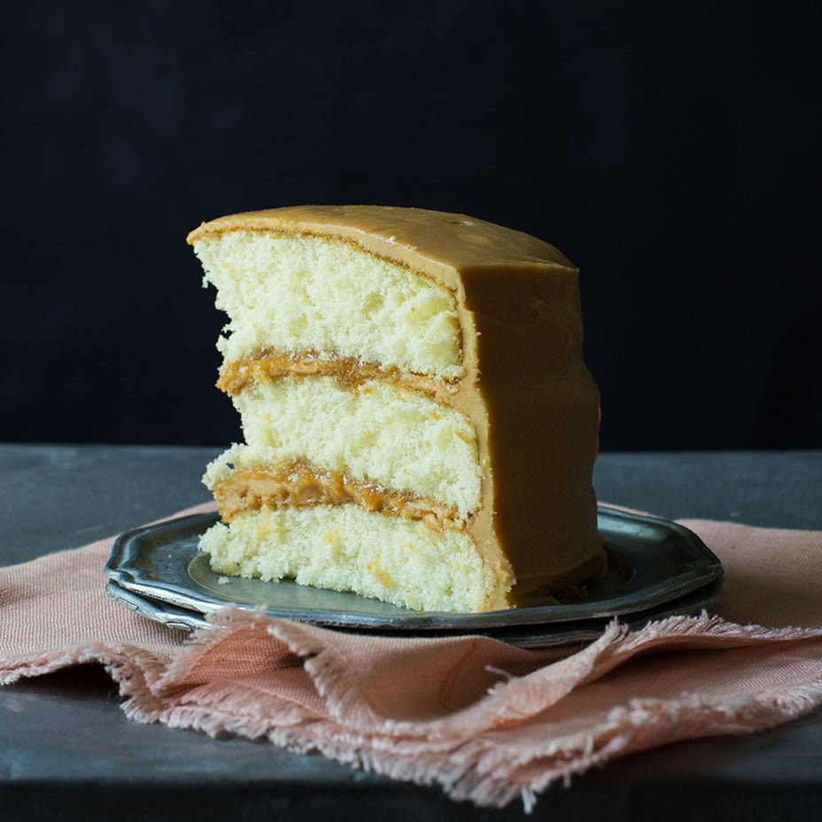 Slice of caramel cake on a concrete countertop and light pink cloth