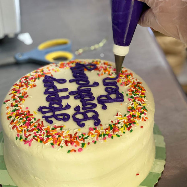Vanilla cake with sprinkles and purple writing that says "Happy birthday, Ben"