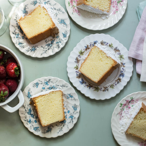 Slices of cream cheese pound cake on white plates with floral prints, next to a bowl of strawberries