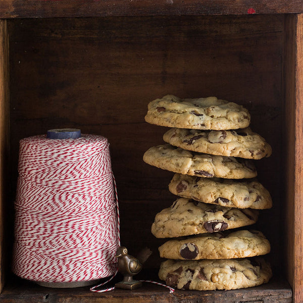 Chocolate chip walnut cookies stacked inside a wooden shelf next to a spool of yarn