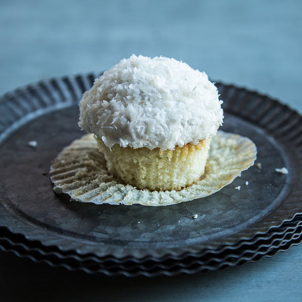 Unwrapped coconut cupcakes on black plates with a blue background