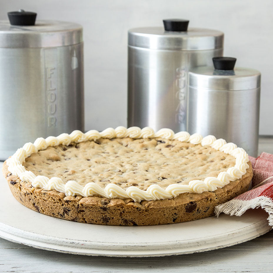 Large chocolate chip cookie on a tray next to stainless steel containers of flour and sugar
