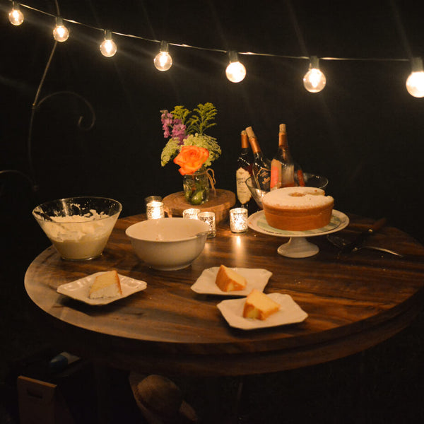 String lights and a table with cakes on it outdoors at night 