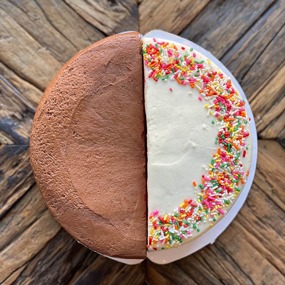 Half of a chocolate cake and vanilla cake with sprinkles on a wooden countertop