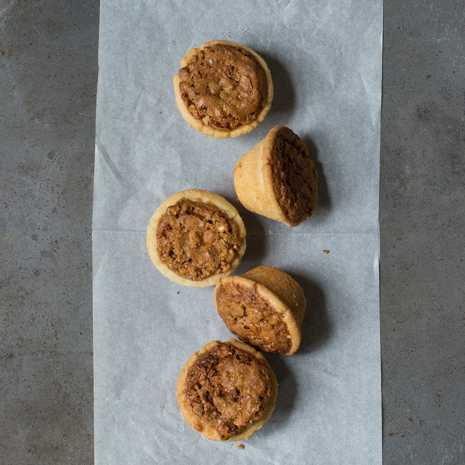 five pecan tassies on parchment sitting on a grey countertop