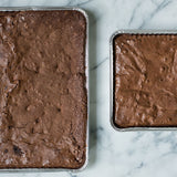 Two different sized trays of plain brownies on a marble countertop