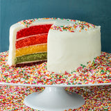 Rainbow cake sitting on a tray covered in rainbow sprinkles
