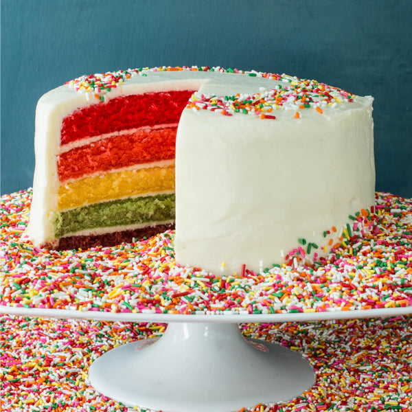 Rainbow cake sitting on a tray covered in rainbow sprinkles