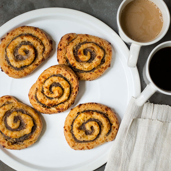 Sausage pinwheels on a white plate next to two cups of coffee