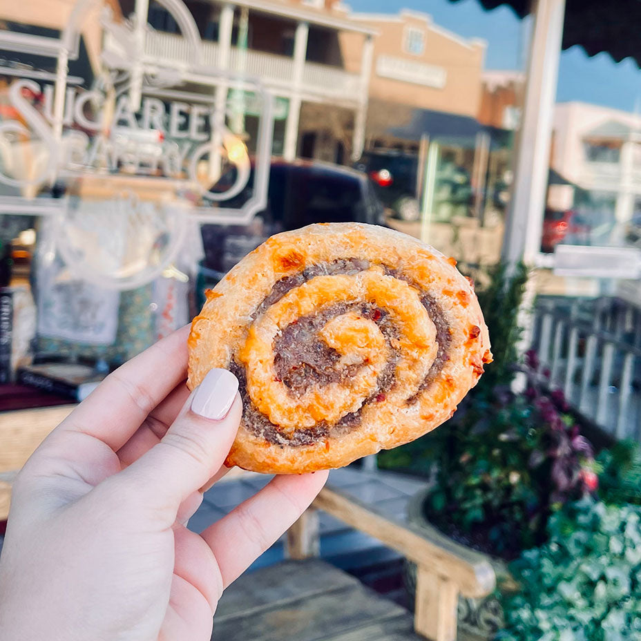 Person holding a sausage pinwheel in front of Sugaree's bakery