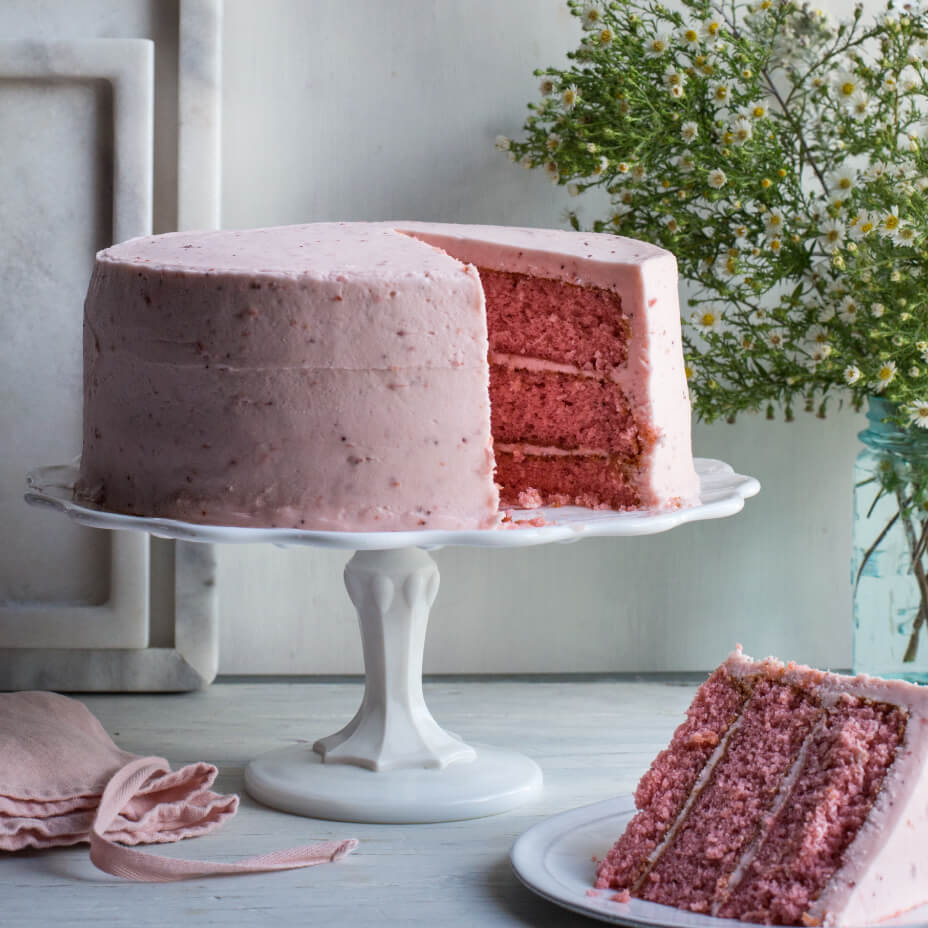 Strawberry cake on a white tray next to a vase of flowers