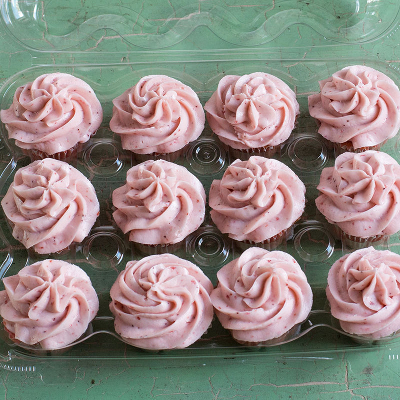 A dozen strawberry cupcakes in a plastic tray on a green countertop
