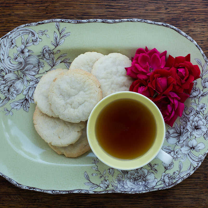 Tea cakes on a flower tray next to a glass of tea and red roses