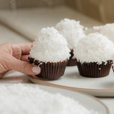 Coconut cupcakes with coconut topping on a white plate, held by a hand