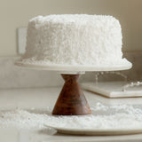 Sugaree’s Coconut Cake on a marble cake stand with a wooden base