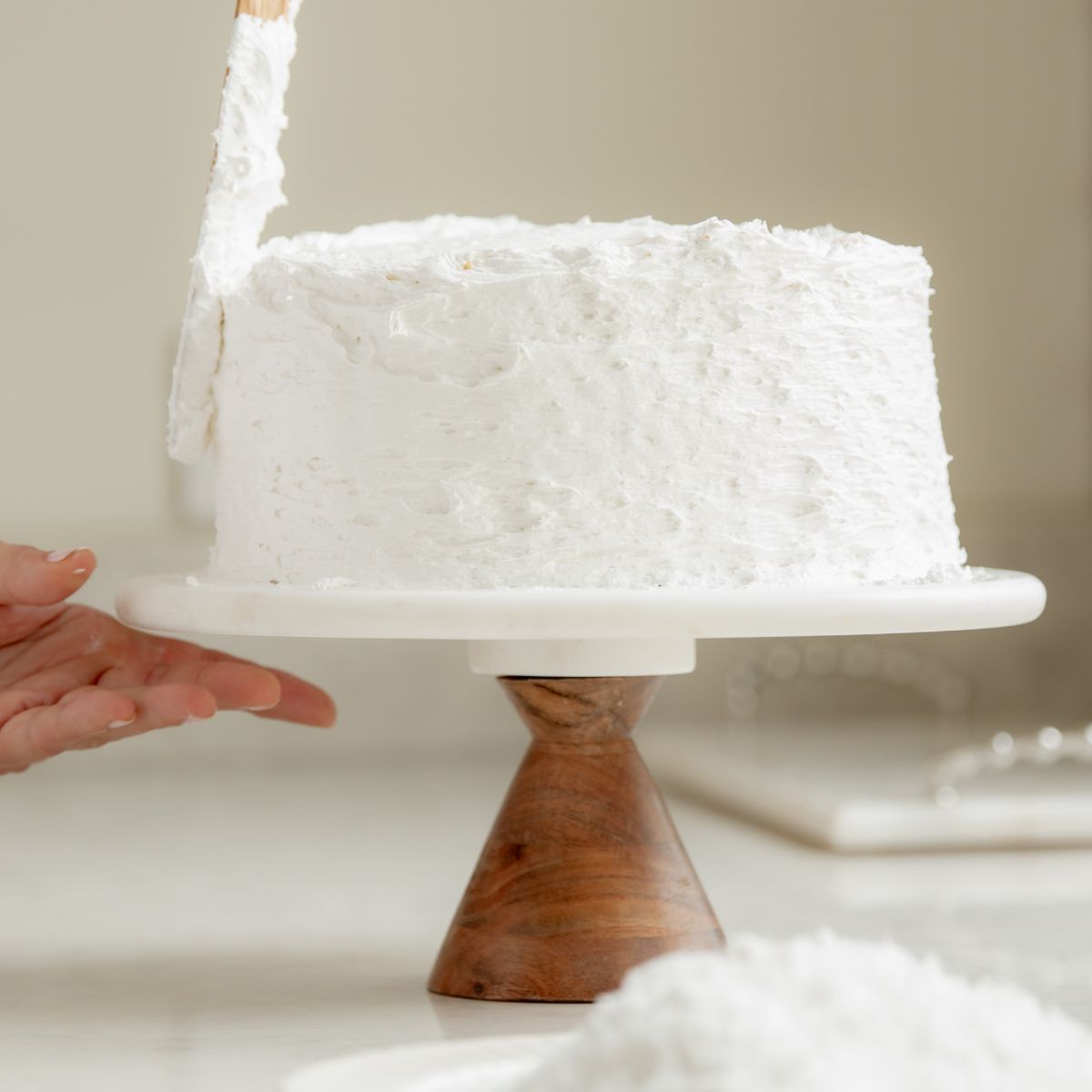 Sugaree’s Coconut Cake being frosted on a cake stand