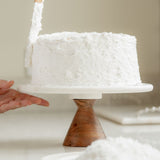Sugaree’s Coconut Cake being frosted on a cake stand