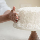 Sugaree’s Coconut Cake being hand-coated in fresh coconut shavings