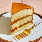Slice of layered Sugaree’s Caremel Cake with caramel filling on a white plate with a gold fork.