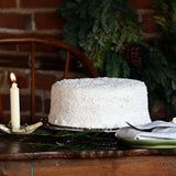 Sugaree’s Coconut Cake on a wooden table with a lit candle and greenery in the background