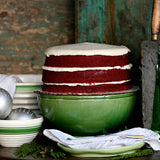 Sugaree’s Red Velvet Cake with white frosting in a green bowl on a rustic holiday background