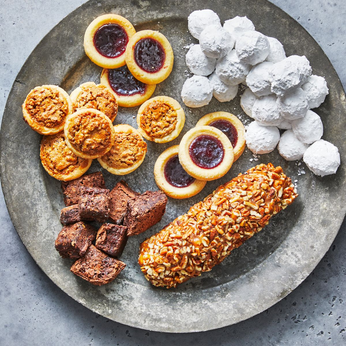 Assorted Sugaree’s small cookies and brownie bites on a round stone platter with a gray background