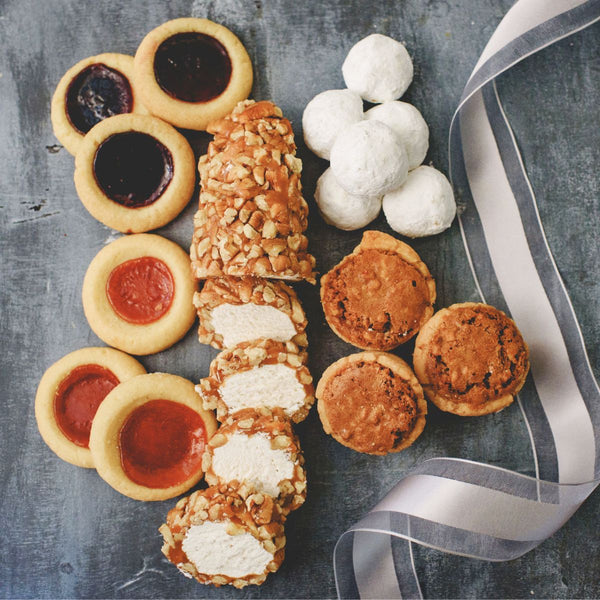 Assorted small Sugaree’s cookies and tarts with a ribbon on a textured surface
