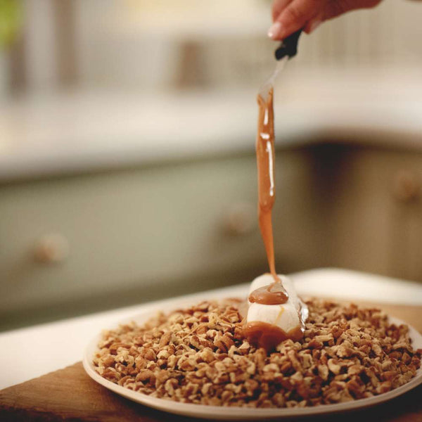 Divinity on a plate of pecans being layered with homemade caramel