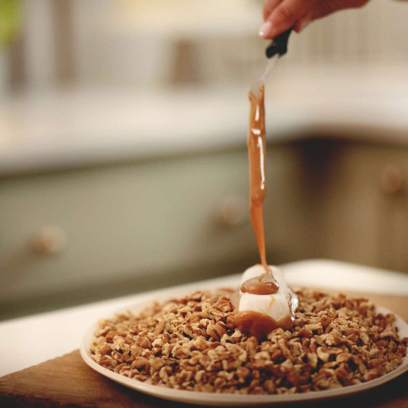 Divinity on a plate of pecans being layered with homemade caramel