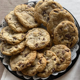 A dessert tray of Sugaree’s Chocolate Chip Cookies stacked on a 12-inch party tray with a white paper doily, set on a light beige tablecloth