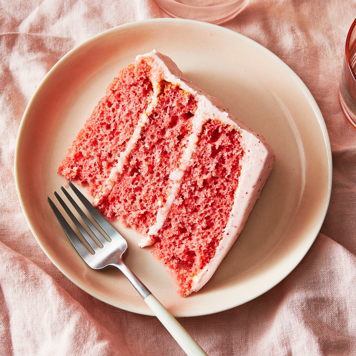 Slice of pink Sugaree’s Strawberry Cake showing three layers on a white plate with a pink tablecloth.