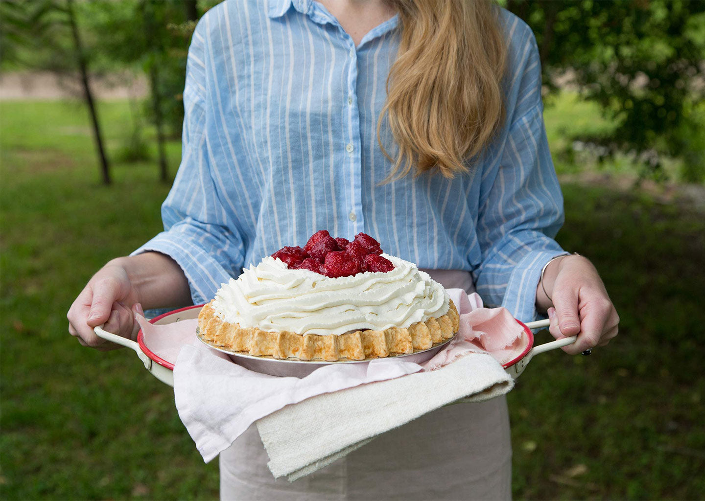 someone holding a tray with a strawberry pie atop pink cloth outside