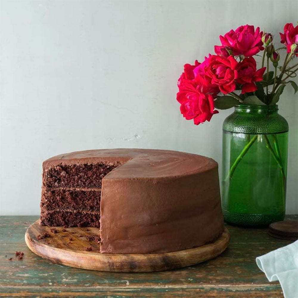 Chocolate cake on a tray next to a green vase with red roses