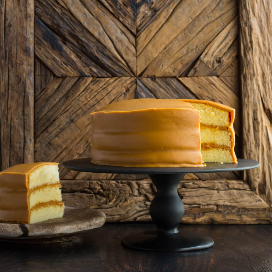 Caramel cake and slice of caramel cake on a metal tray with wooden background