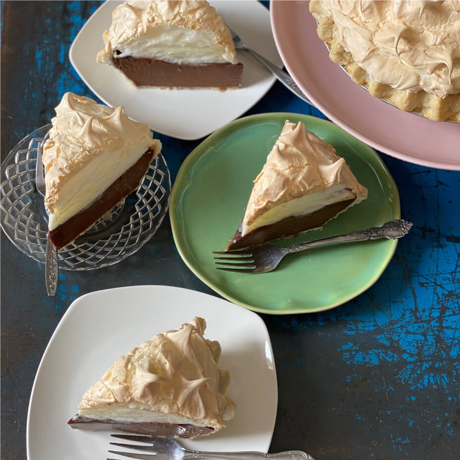 Slices of chocolate meringue pie on a blue countertop with different colored plates