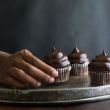 Three ding dong cupcakes on tray and person's hand is lifting up one