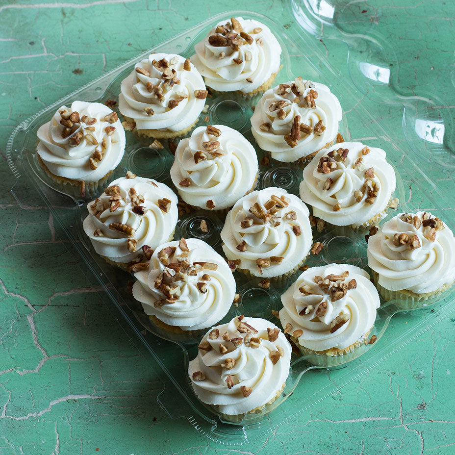A dozen Italian cream cupcakes in a plastic tray on a green countertop