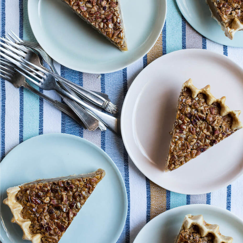 Slices of pecan pie on blue and pink plates atop a striped tablecloth