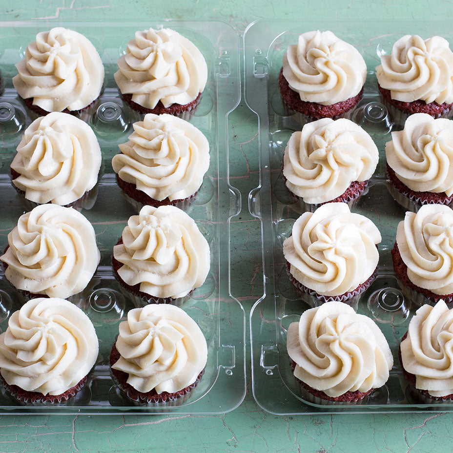 Two plastic trays of Red Velvet Cupcakes on a green countertop