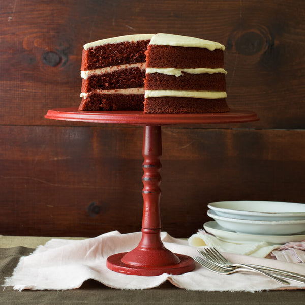 Red velvet cake on a red cake stand in front of a wooden wall