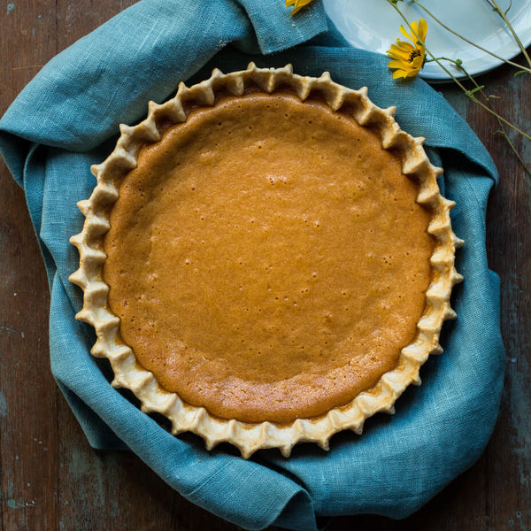 Sweet potato pie on a blue cloth next to yellow flowers