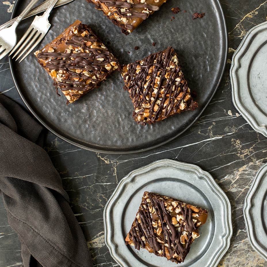 Turtle brownies on dark gray and light gray plates with silverware